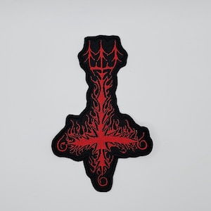 May include: Black and red embroidered patch featuring an inverted cross design. The patch has a detailed, flame-like pattern in red against a black background. The patch is likely for clothing or accessories.