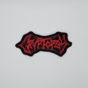 Op de afbeelding: Een zwart embleem met rode geborduurde tekst "CRYPTOR". De patch heeft een grillige rand. De tekst is in een gotisch lettertype, vaak geassocieerd met heavy metal muziek.