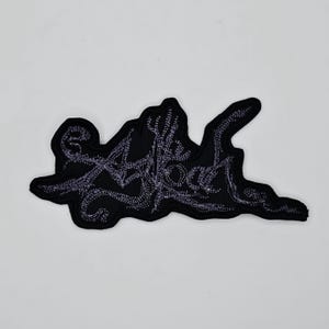 Puede incluir: Parche bordado negro con el texto "Alive Today" en una escritura estilizada. El parche tiene un fondo oscuro y el texto es de un color más claro, creando un contraste. Para ropa o accesorios.