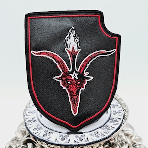 May include: A black embroidered patch with a red outline, depicting a red goat head with horns and a pentagram on its forehead. The goat head is surrounded by three flames.