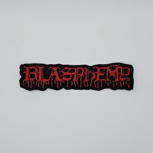 May include: A black embroidered patch featuring the word "BLASPHEMY" in red, dripping font. The patch is rectangular with a black border. The text is stylized and has a dripping blood effect.
