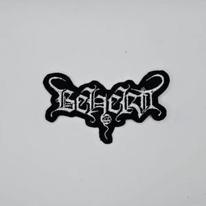 Op de afbeelding: Zwart en wit geborduurde patch met het woord "Beherit" in een gotisch lettertype. De patch heeft een zwarte rand en een wit geborduurd ontwerp. De patch is bedoeld voor kleding of accessoires.