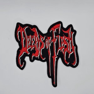 May include: A black patch featuring the text "DEEDS OF FLESH" in red, outlined in white. The patch has an unusual shape and is designed for application on clothing or accessories.