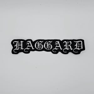May include: Black embroidered patch with the word "HAGGARD" in white gothic lettering. The patch has a black border and is rectangular in shape. The patch is likely for clothing or accessories.