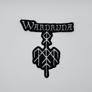 May include: Black and white embroidered patch featuring the word "WARDRUNA" above a stylized symbol. The patch has a unique shape and design, suitable for application on clothing or accessories.