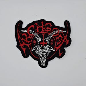 May include: Embroidered patch with a black background and a red and white design. The design features a goat skull with long horns, surrounded by red, stylized, gothic lettering and symbols. The patch has a black border.