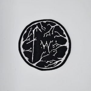 Op de afbeelding: Zwart en wit geborduurde patch met een cirkelvorm. De patch heeft een wit ontwerp op een zwarte achtergrond. Het ontwerp bevat een kruisachtig symbool en de letters "MY" in een netwerk van witte lijnen.