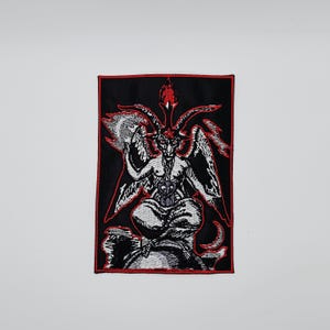 Puede incluir: Parche bordado con una ilustración detallada de Baphomet, una deidad con cabeza de cabra, en blanco y gris sobre un fondo negro. El parche tiene un borde rojo. La imagen representa a Baphomet sentado, con alas, cuernos y una antorcha.