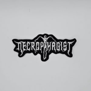 Puede incluir: Parche bordado en blanco y negro con la palabra "NECROPHAGIST" en una fuente gótica. El parche presenta una figura estilizada en el centro. El parche es probablemente para una chaqueta o bolso, y es un símbolo del género musical death metal.