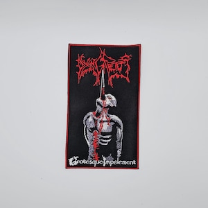 Peut inclure: Écusson rectangulaire noir avec une bordure rouge. Il présente un graphisme blanc d'une figure empalée par une pointe, avec des détails de sang rouge. L'écusson porte le texte "Dying Fetus" et "Grotesque Impalement" en rouge.