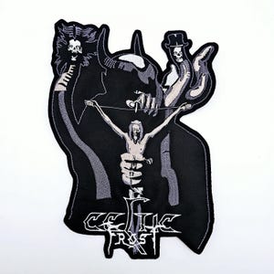 May include: Embroidered black and white patch with a gothic design. It depicts a skeletal figure on a cross, held by a horned demon. The patch features the band name "CELTIC FROST" in a decorative font, ideal for clothing.