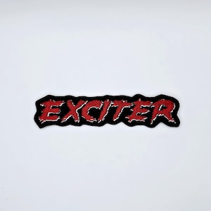May include: A black embroidered patch featuring the word "EXCITER" in red, distressed lettering. The patch has a black border with white stitching. The rectangular patch is set against a white background.