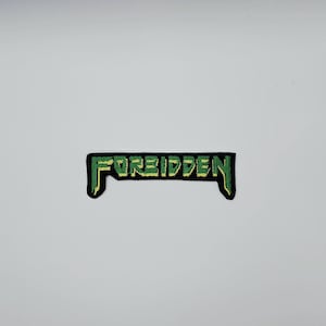 May include: A rectangular patch with the word "FORBIDDEN" embroidered in green and yellow thread on a black background. The patch has a unique shape with pointed edges.