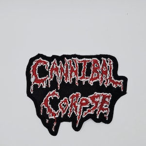 May include: Black embroidered patch with the band name "CANNIBAL CORPSE" in red, dripping-style lettering. The patch has a black border and is designed for application on clothing or accessories.