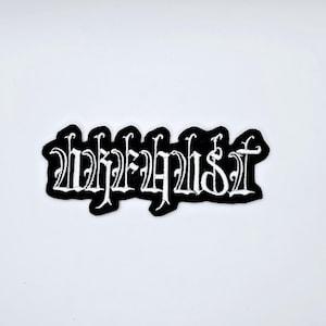 Puede incluir: Un parche bordado en blanco y negro con la palabra "Whalefist" en una fuente gótica. El parche tiene un borde negro y está sobre un fondo blanco. El texto está en una fuente estilizada y decorativa.