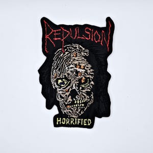 Może przedstawiać: Biały ceramiczny kubek z czarnym uchwytem i napisem "But First, Coffee" w stylu odręcznym. Kubek prawdopodobnie mieści 350 ml i stoi na białej powierzchni.