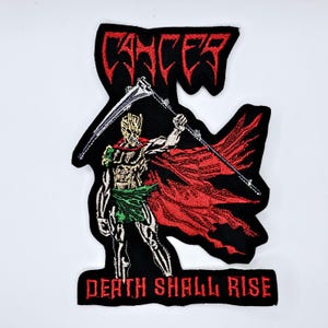 May include: Embroidered patch with a figure holding a scythe, wearing a red cape, and the text "CANCER" and "DEATH SHALL RISE" in red. The patch is black with detailed stitching on a white background.