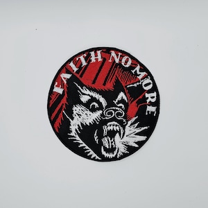 Könnte beinhalten: Ein runder, schwarzer Aufnäher mit den Worten "FAITH NO MORE" in Weiß, oben gewölbt. Eine knurrende Wolfsgrafik in Schwarz und Weiß ist zentriert, mit roten Streifen im Hintergrund.