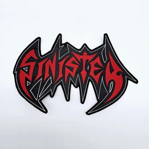 May include: A red and black patch with the word "SINISTER" in a stylized font. The text is red with a black outline and a white border. The patch has a jagged, irregular shape.