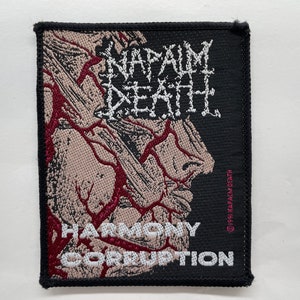 Peut inclure: Patch brodé noir avec le nom du groupe "Napalm Death" en lettres blanches et le titre de l'album "Harmony Corruption" en lettres blanches sur fond rouge. Le patch présente un graphique d'un visage avec des veines rouges.