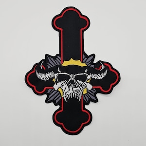 May include: Embroidered black cross patch with a red border, featuring a skull with horns and a yellow crown. The skull has white teeth and is surrounded by gray and yellow accents.