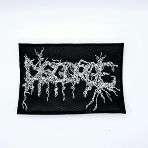 May include: Black rectangular patch with white embroidered text. The text is in a stylized, gothic font. The patch is likely for clothing or accessories.