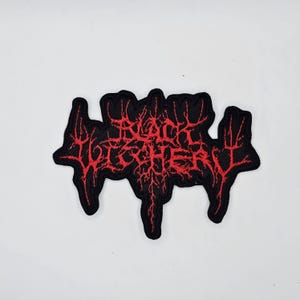 May include: Black Witchery embroidered patch with red text on a black background. The text is in a stylized, gothic font. The patch has a unique, irregular shape, and is likely designed to be sewn onto clothing or accessories.