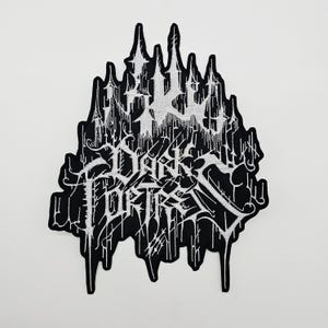 Könnte beinhalten: Schwarz-weißer gestickter Aufnäher mit dem Text "DARK FORTRESS" in einer gotischen Schriftart. Der Aufnäher hat oben ein burgähnliches Design und tropfende Akzente.