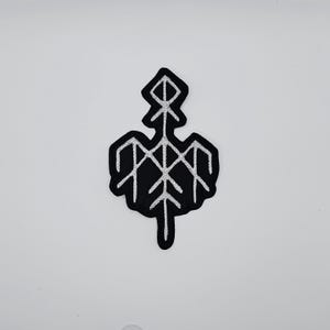 May include: Black embroidered patch featuring a white geometric design. The patch has a unique shape with a central vertical line and a series of intersecting lines, resembling a stylized bird or symbol. The patch is likely for clothing or accessories.