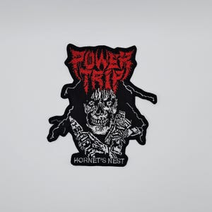 May include: Black and white embroidered patch featuring a skull with a lightning bolt design. The patch has the words "POWER TRIP" in red and "HORNET'S NEST" in white.