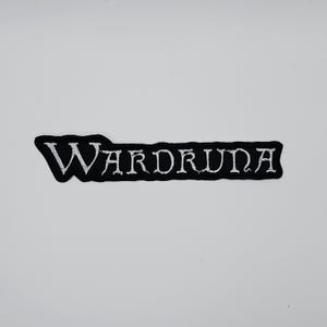 May include: Black embroidered patch with the word "Wardruna" in white, stylized lettering. The patch has a black border and is set against a white background. The text is the focal point of the patch.