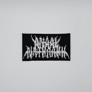 Puede incluir: Parche rectangular negro con texto blanco bordado en una fuente gótica. El texto parece ser el nombre o logotipo de una banda. El parche es probablemente para una chaqueta, bolso u otra prenda.