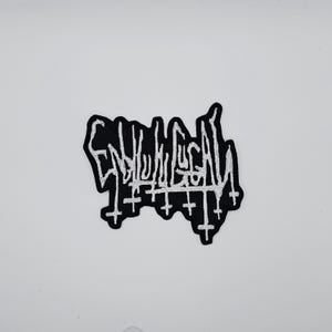 Op de afbeelding: Zwart en wit geborduurde patch met het woord "ENLIGHTEN" in een gestileerd, gotisch lettertype. De patch heeft een reeks omgekeerde kruisen aan de onderkant. De patch staat op een witte achtergrond.