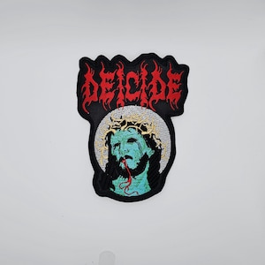 May include: Embroidered patch featuring the word "DEICIDE" in red, flame-like lettering above an image of a teal-skinned figure wearing a crown of thorns. The figure has a bloody mouth and is set against a white background.