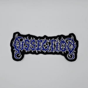May include: A black patch with the word "DISSECTION" embroidered in blue, outlined in white. The lettering has a gothic, stylized design. The patch has a black border and is likely for clothing or accessories.