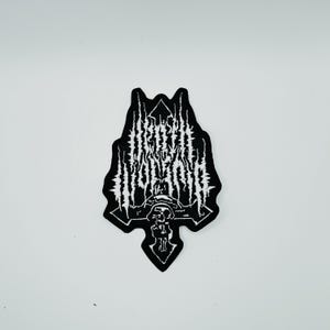 Op de afbeelding: Een zwart-witte geborduurde patch met de tekst "DEATH WORSHIP" in een grillig, gestileerd lettertype. Het ontwerp bevat een centrale kruisvorm met een schedelmotief aan de basis, alles omlijnd met zwart garen op een witte achtergrond.