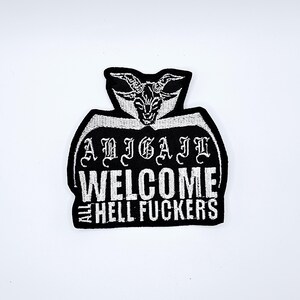 May include: Black and white embroidered patch with the text "ABIGAIL WELCOME ALL HELL FUCKERS". The patch features a goat head design at the top.