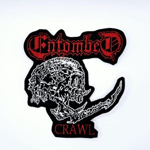 May include: Embroidered black patch featuring a white skull design with a curved blade and the word "CRAWL" in red. The patch also includes the word "Entombed" in red, gothic-style lettering.