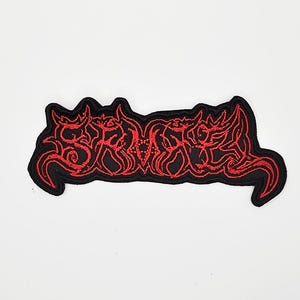 May include: Embroidered patch with a black border and red, stylized text. The text appears to be a band logo or similar design, with a gothic or heavy metal aesthetic. The patch is rectangular with curved edges.