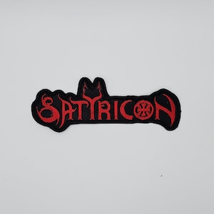 Op de afbeelding: Zwart geborduurde patch met het woord "SATYRICON" in rode, gestileerde letters. De patch heeft een unieke vorm en bevat een symbool aan het einde. De patch is waarschijnlijk voor een band of muziekgerelateerde merchandise.