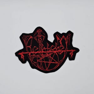 Può includere: Toppa ricamata nera e rossa con un design gotico. La toppa presenta un pentagramma e altri simboli in filo rosso su sfondo nero. La toppa è probabilmente per abbigliamento o accessori.