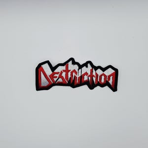 Puede incluir: Parche bordado con la palabra "Destruction" en letras rojas estilizadas. El parche tiene un borde negro y un fondo blanco para las letras. Probablemente está diseñado para coser en ropa o bolsos.