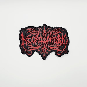 May include: Black and red embroidered patch with a gothic design. The patch features stylized, ornate text in red against a black background. The patch has a unique shape with pointed edges and a decorative border.
