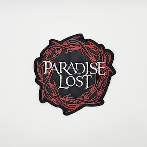 May include: Embroidered patch with the words "PARADISE LOST" in white script on a black background. The text is surrounded by a red, thorny wreath design. The patch has a black border.