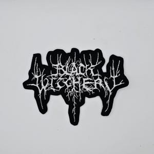 Op de afbeelding: Zwarte patch met de witte tekst "BLACK LEATHER" in een gotisch lettertype. Het ontwerp bevat een zwarte rand en een gedetailleerd wit patroon in de letters, dat doet denken aan boomtakken. Geschikt voor kleding of accessoires.