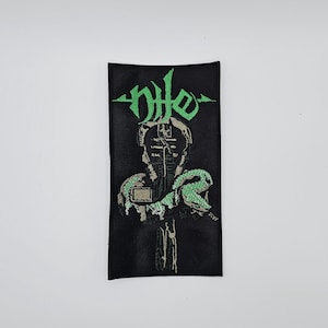 May include: Black rectangular patch with the word "nhe" in green, stylized lettering at the top. Below the text is a detailed illustration of a figure with a snake wrapped around it. The snake and figure are in shades of green and gray.