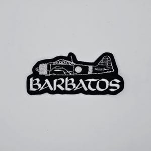 Peut inclure: Écusson brodé noir et blanc représentant un avion et le mot "BARBATOS". Le patch a une bordure noire et est posé sur un fond blanc.