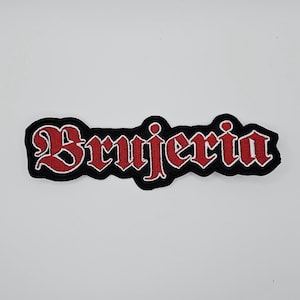 May include: Embroidered patch with the word "Brujeria" in red gothic lettering, outlined in white, on a black background. The patch has a black border and is likely for clothing or accessories.