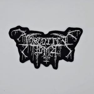 May include: Black embroidered patch with the text "FORGOTTEN BOY". The text is in a gothic, stylized font with white thread. The patch has a unique, irregular shape and is likely for clothing or accessories.