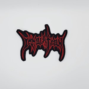 May include: A black patch featuring the red embroidered text "MORTAL DOOM" in a distinctive, stylized font. The patch has a black border. It is designed to be sewn or ironed onto clothing or accessories.